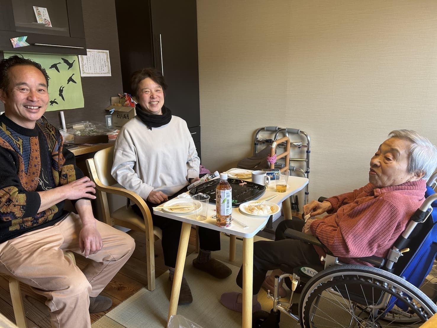 入居者と職員がテーブルを囲んで食事・交流する風景。明るい共用スペース。
